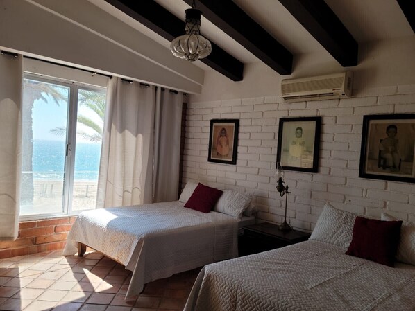 A room with two beds, a large window with curtains, a brick wall, and framed pictures. - Beautiful beachfront 7 BR 6.5 BtR colonial style estate on 30,000 sqft lot (Kino Nuevo)