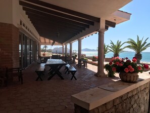 Un patio al aire libre con mesas y sillas, un muro de piedra y vista al mar.