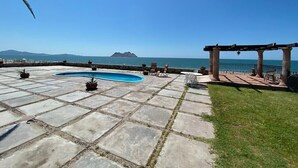 Un área de piscina con baldosas de piedra, una pérgola y vistas al mar y a las montañas.