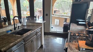 A modern kitchen with a granite countertop, stainless steel appliances, and a view of the outdoor area through large windows.