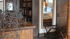 A room with a wooden desk, a bookshelf, a mirror, and a bed with a patterned bedspread.