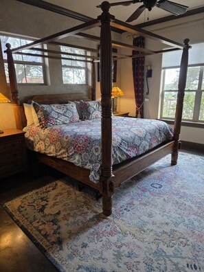Un lit à baldaquin avec une couvre-lit à motifs, un plancher en bois et une grande fenêtre avec des rideaux.