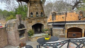 An outdoor patio with stone-built fireplaces, a round table, and a patterned bench.