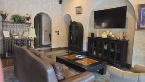 Un salon spacieux avec un canapé en cuir, une table basse et un téléviseur à écran plat fixé au mur.