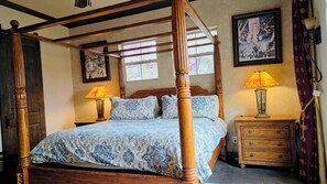 Una cama con dosel, un edredón estampado, dos lámparas de noche, una mesita de madera y un cuadro en la pared.