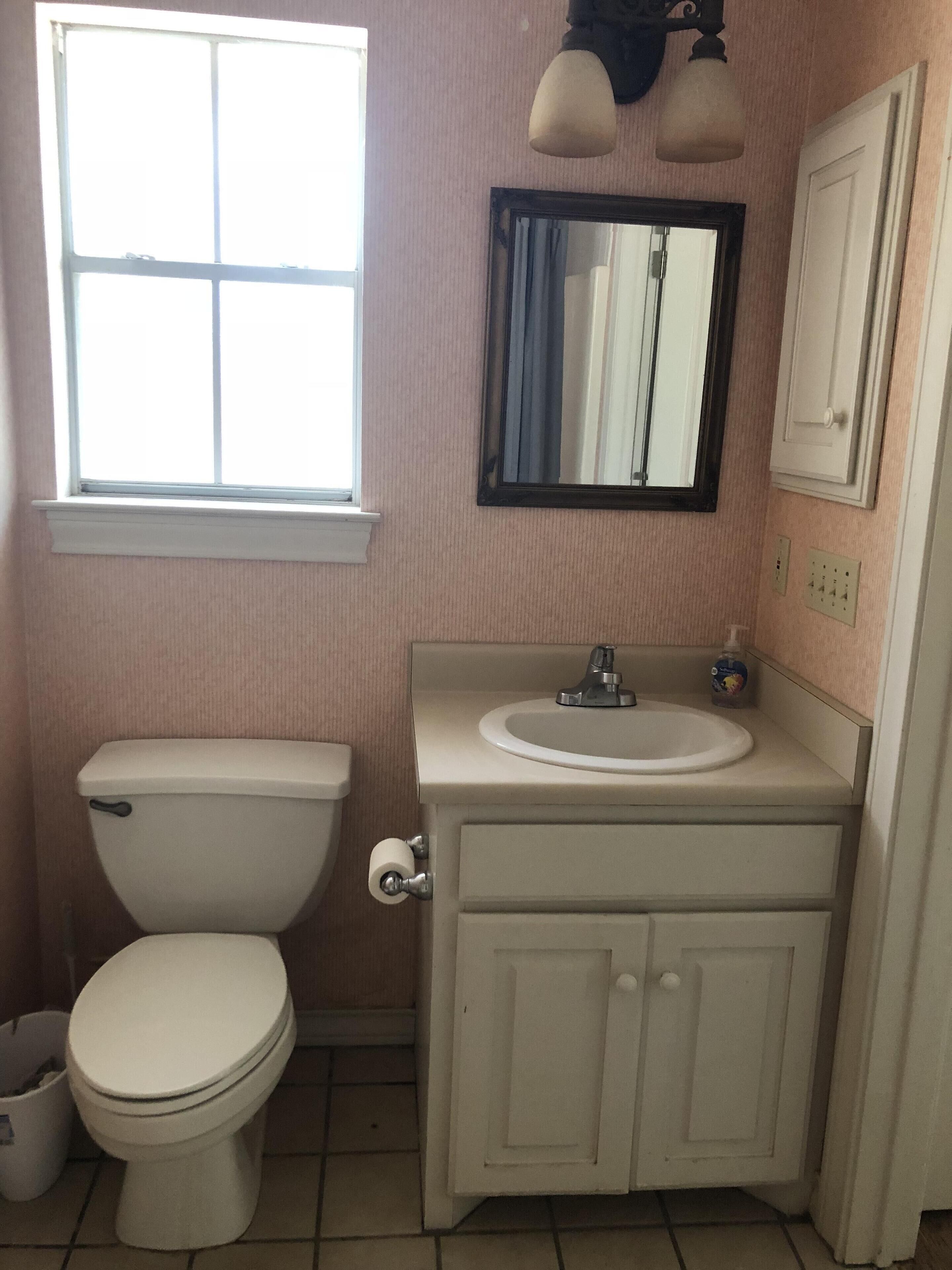 A bathroom with a toilet, sink, mirror, and cabinet.