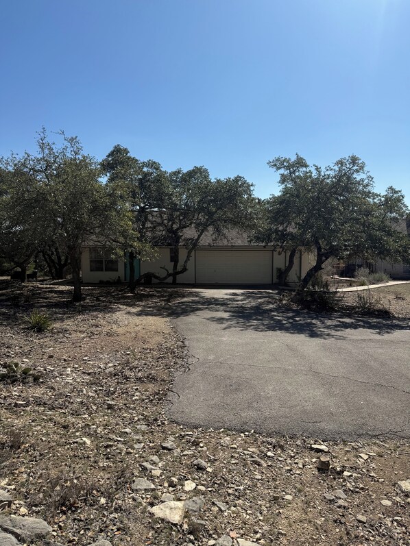 A building with a garage door, surrounded by trees and a gravel driveway.