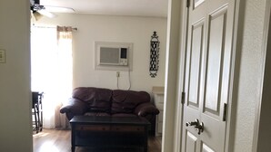 Un couloir mène à un salon où se trouvent un canapé en cuir marron et une table basse en bois foncé.