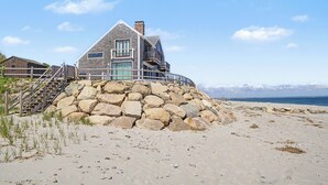 A beachfront house with a stone foundation, a balcony, and a staircase leading to the entrance. - 14 Captain Crocker (East Sandwich)
