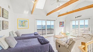 A room with two beds, a sofa, a table, and a view of the beach. - 14 Captain Crocker (East Sandwich)