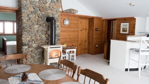 Une pièce chaleureuse avec un mur en pierre, un lambris en bois, une cheminée, une table à manger avec des chaises et un petit coin cuisine.