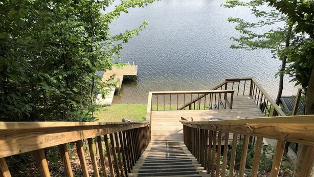 Un escalier en bois descend vers une jetée au bord d’un lac, le tout étant entouré d’arbres.