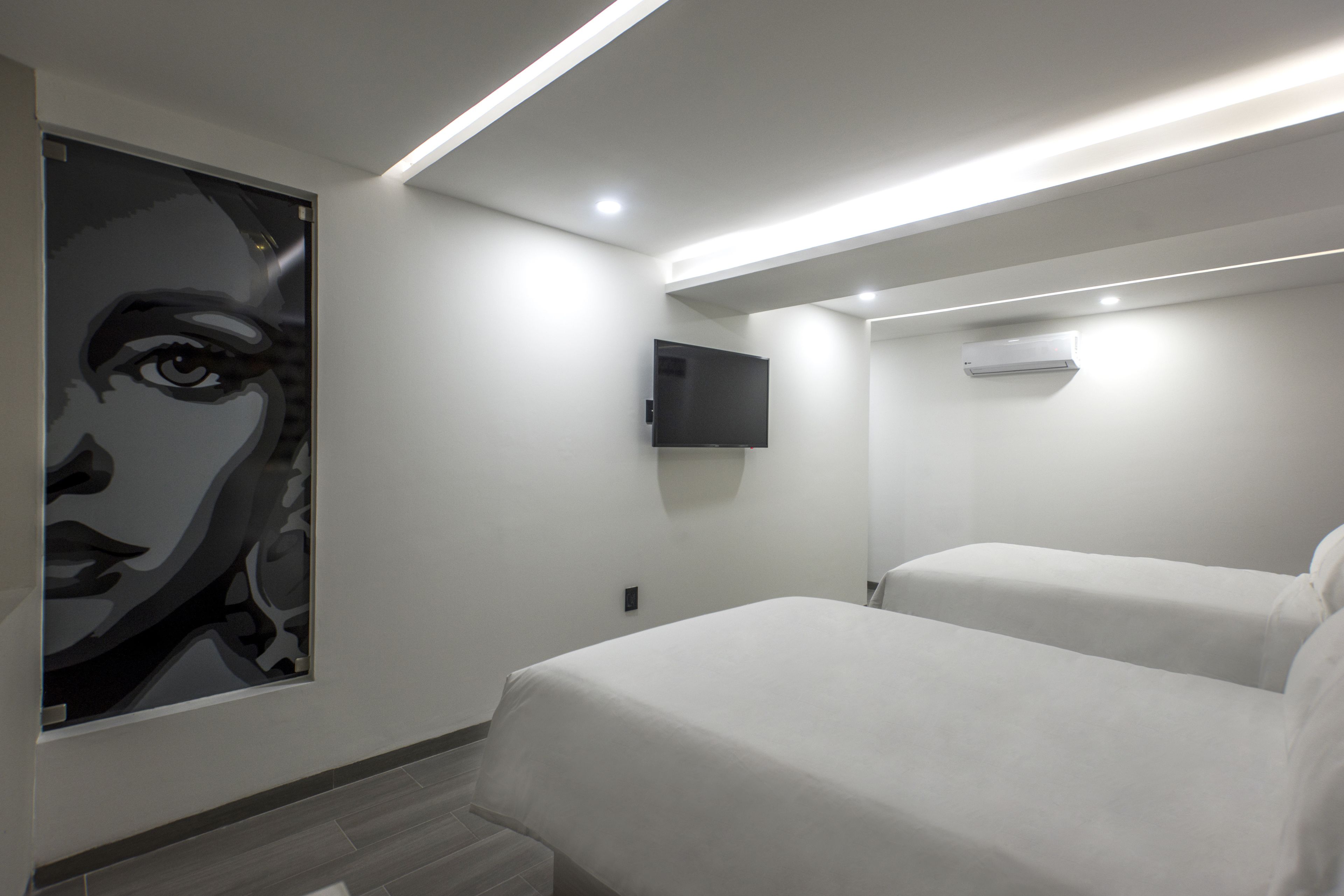 A modern hotel room with a large bed, a flat-screen TV mounted on the wall, and a ceiling-mounted air conditioning unit.