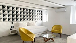 A modern hotel room with a white bed, two yellow armchairs, a glass coffee table, and a geometric-patterned wall. - La Casona que Encanta (Querétaro)