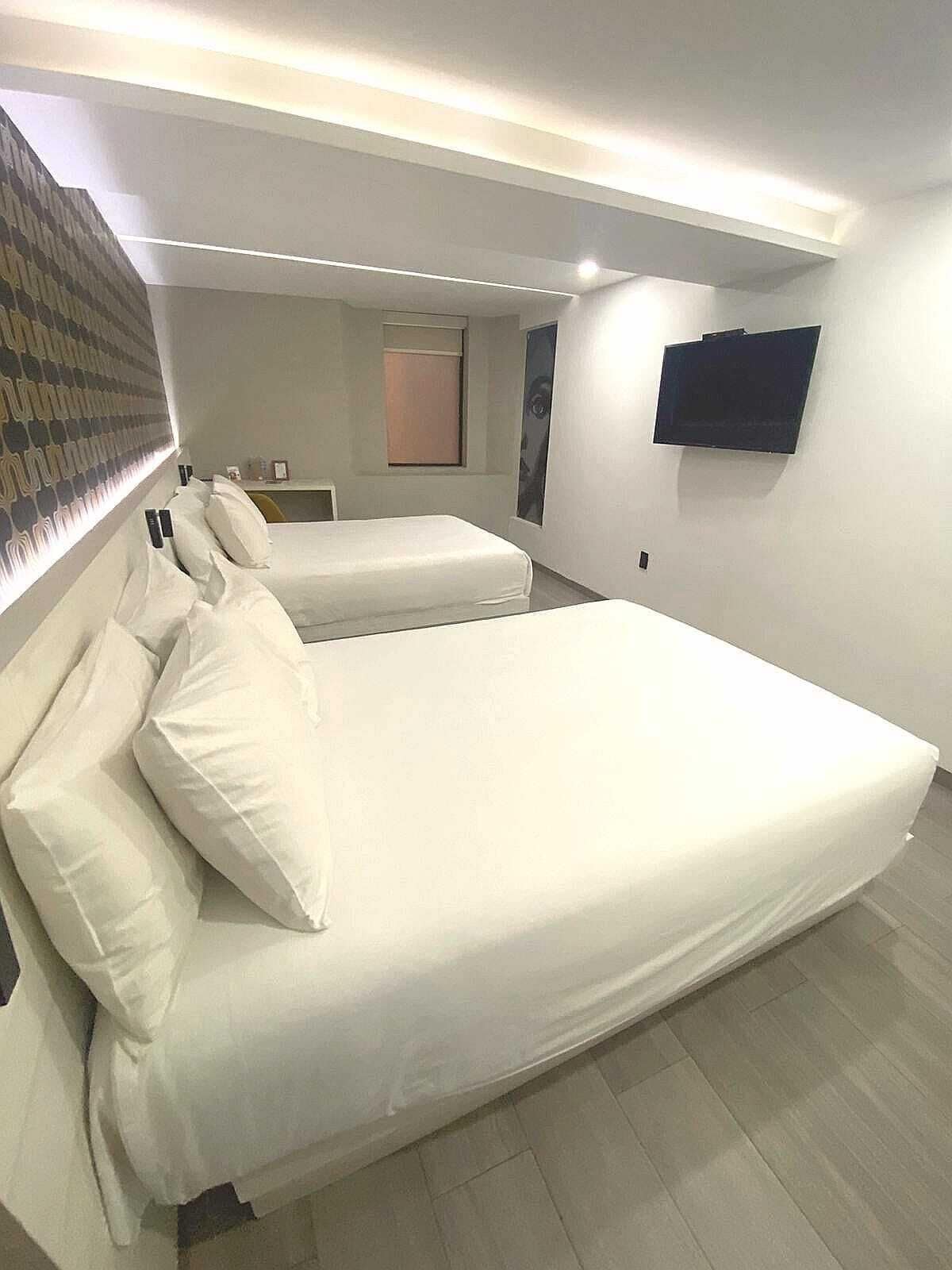 Une chambre d’hôtel moderne équipée de deux lits simples, d’un téléviseur à écran plat fixé au mur et d’un petit coin salon avec une table et des chaises.