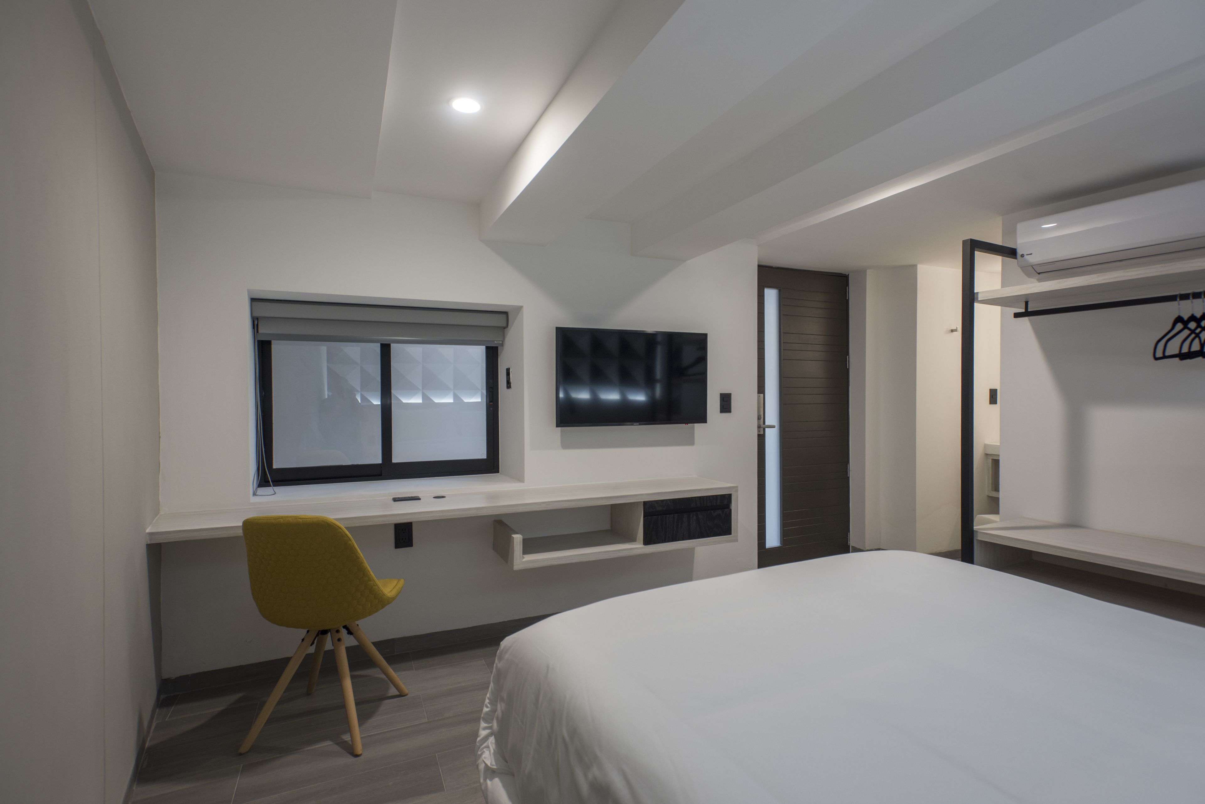 A modern bedroom with a bed, a desk with a chair, a TV, and a wardrobe.