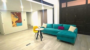 A modern living room with a teal sofa, a small round table, and a painting on the wall. - La Casona que Encanta (Querétaro)