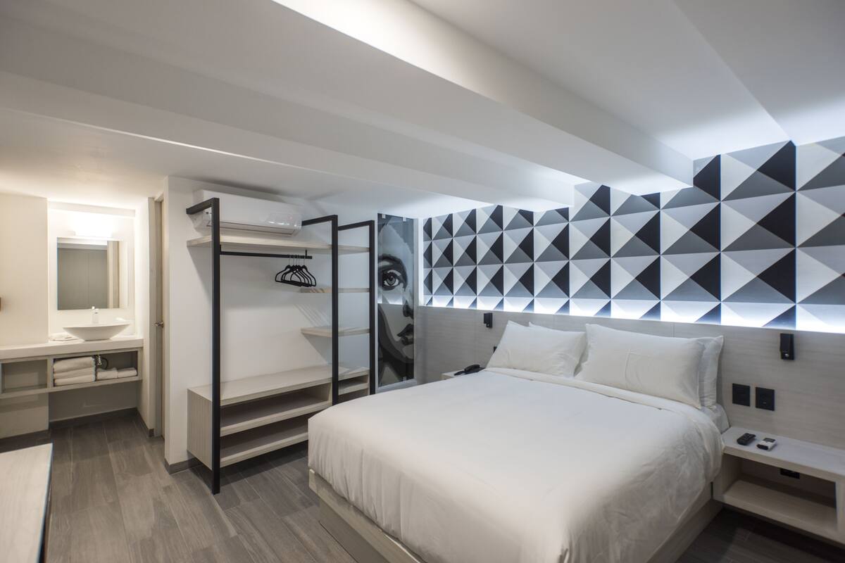 A modern hotel room with a large bed, a vanity with a mirror, and a geometric-patterned wall.