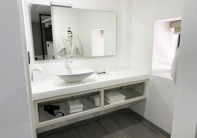 Un baño moderno con lavamanos, espejo y tocador blancos. Hay toallas y un secador de pelo en el tocador.