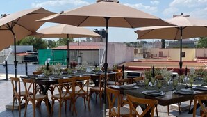 An outdoor dining area with multiple tables and chairs, large umbrellas, and a view of the cityscape. - La Casona que Encanta (Querétaro)