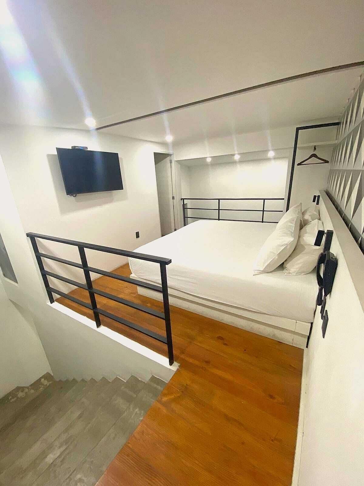 A bedroom with a bed, a TV mounted on the wall, and a wooden floor.