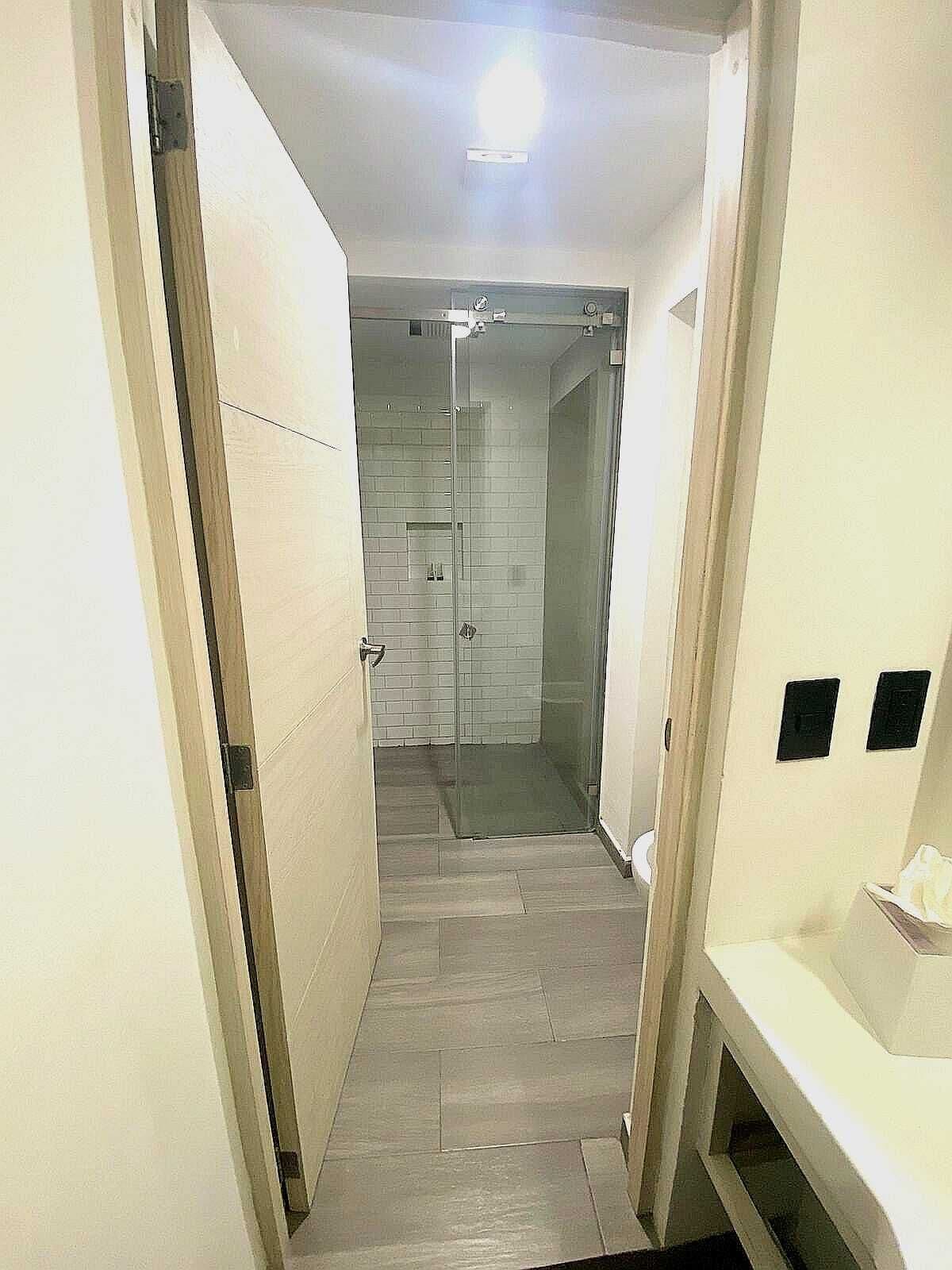 A narrow hallway leading to a bathroom with a glass shower enclosure, tiled walls, and a bench.