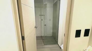 A narrow hallway leading to a bathroom with a glass shower enclosure, tiled walls, and a bench.
