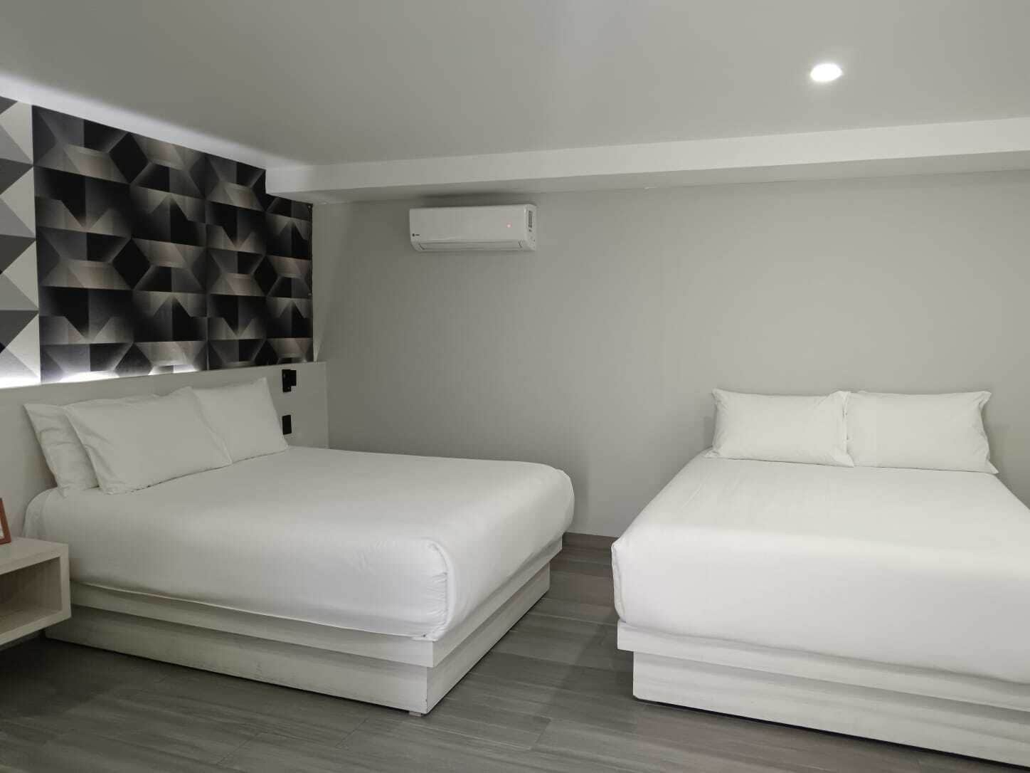 A modern hotel room with two single beds, a geometric-patterned headboard, and a built-in air conditioning unit.