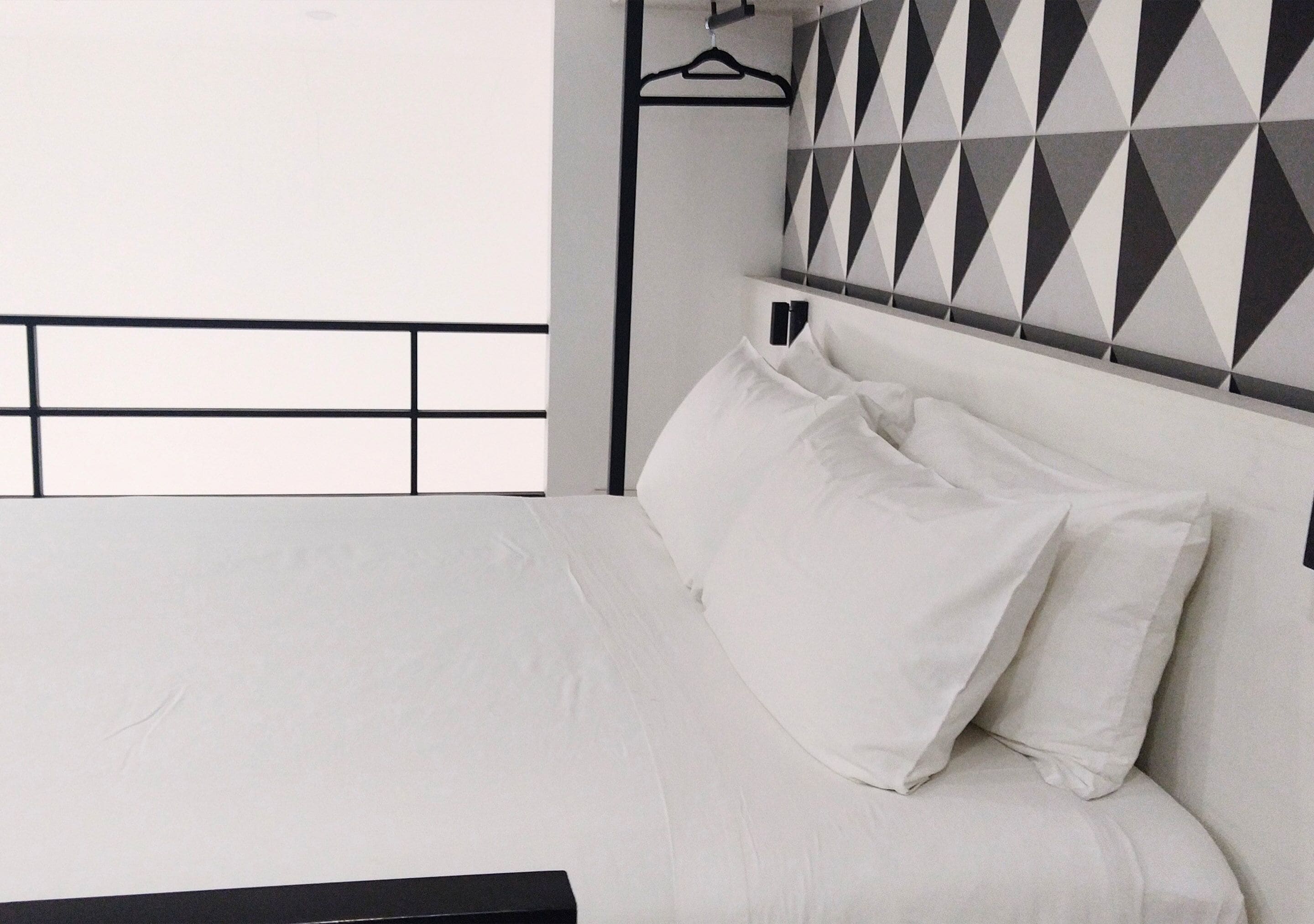 Un lit avec une literie blanche, une tête de lit noire et un mur orné d’un motif géométrique derrière.