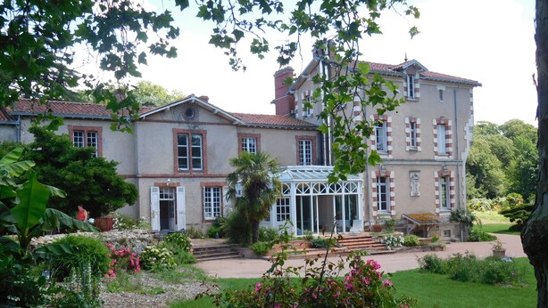 A large, multi-story building with a traditional architectural style, featuring a conservatory and a well-maintained garden with flowering plants. - Large Italian villa with its park, swimming pool and tennis court (Saint-Étienne-De-Mer-Morte)