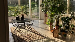 A conservatory with a table and chairs, surrounded by potted plants and a large window. - Large Italian villa with its park, swimming pool and tennis court (Saint-Étienne-De-Mer-Morte)