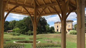 A wooden pavilion with a view of a large building and a pond in the background. - Large Italian villa with its park, swimming pool and tennis court (Saint-Étienne-De-Mer-Morte)
