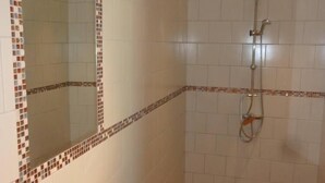 Un bagno con doccia in piastrelle, un lavandino con specchio e pavimento piastrellato.