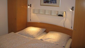 Un dormitorio con dos camas, un armario de madera, un cuadro enmarco y lámparas de noche.