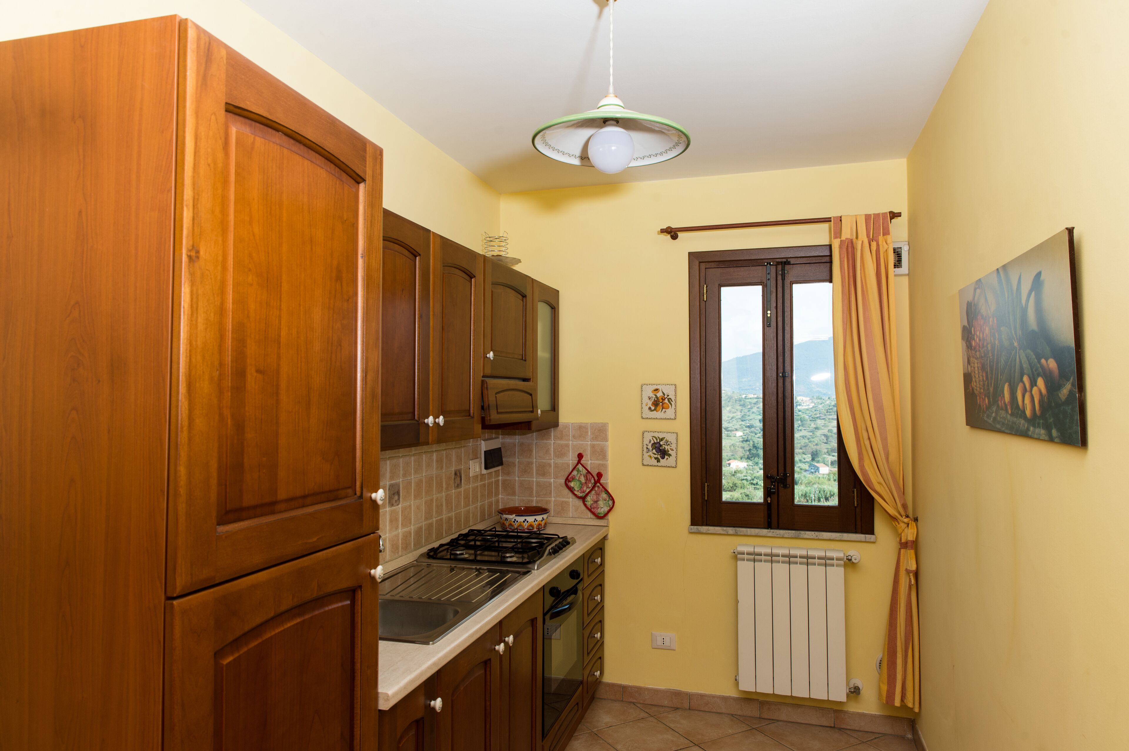 A kitchen with wooden cabinets, a gas stove, a window with curtains, and a radiator.