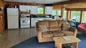 A cozy cabin interior with a kitchenette, a sofa, and a dining area. - Beautiful Lakefront Cottage with Mountain Views (Dedham)