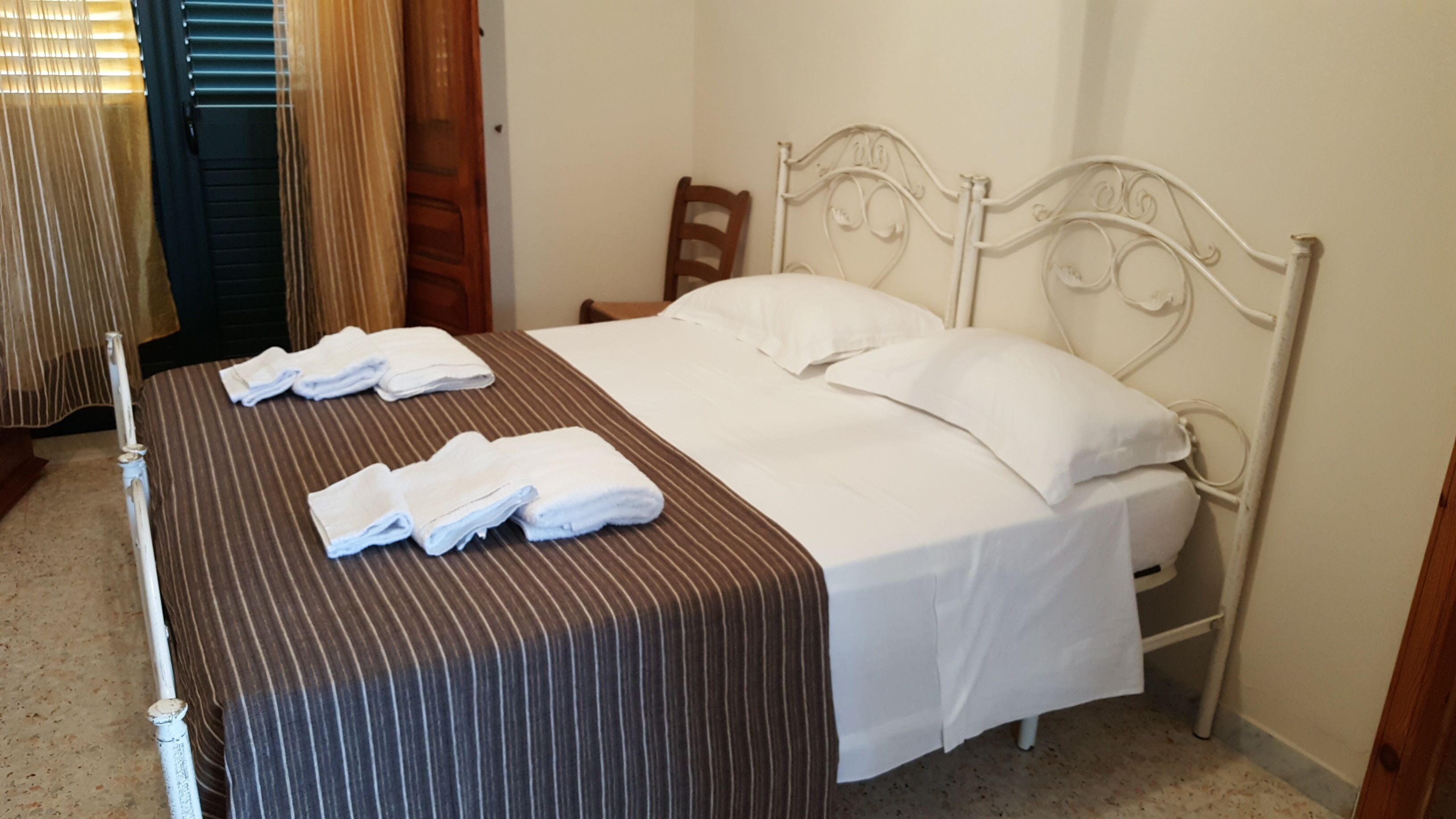 Un letto ben rifatto con lenzuola bianche e una coperta marrone a righe.