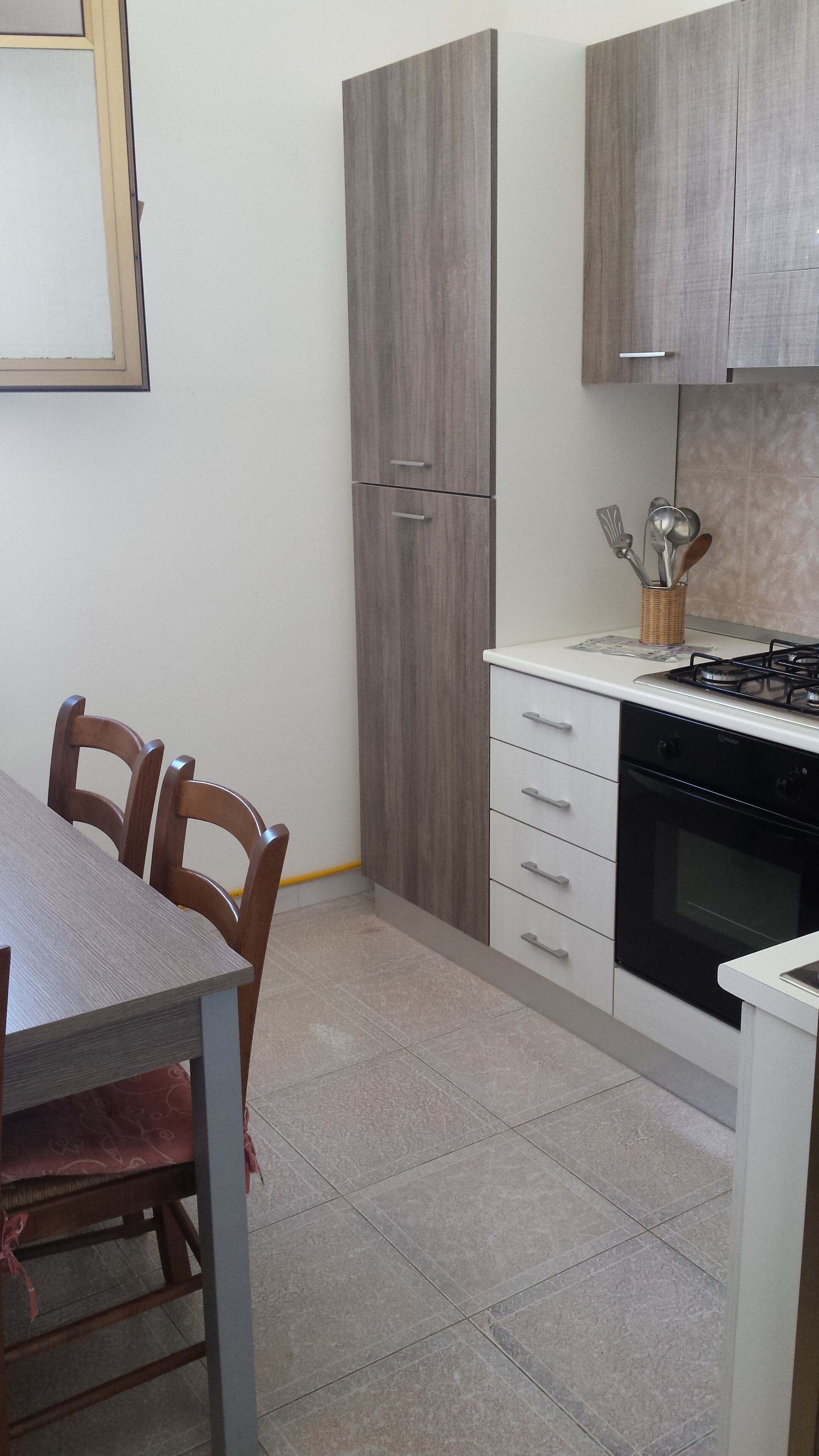 A kitchen with a gas stove, oven, and white cabinets. There is a dining table with chairs and a window above the cabinets.
