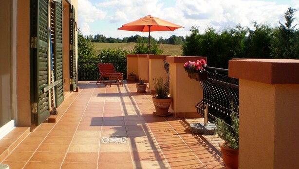A sunlit patio with a red umbrella, a chair, potted plants, and a view of the countryside.