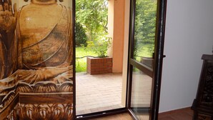 A room with a large Buddha statue, a sliding glass door leading to a balcony with a brick planter, and a wooden cabinet.