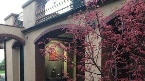 A building with a covered patio area, a brick pathway, and a tree with pink leaves in the foreground.