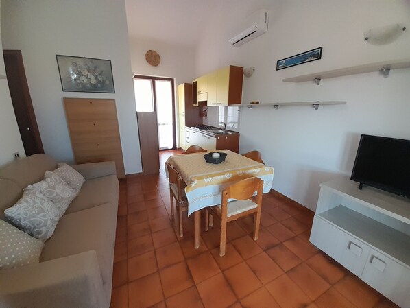 A compact living space with a dining table, chairs, a sofa, a TV, and a kitchen area.