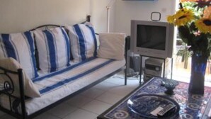 A living room with a sofa, a television, and a table with a vase of flowers.