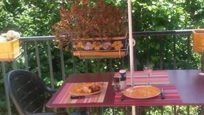 An outdoor patio with a table and chairs under a pink umbrella, surrounded by greenery.