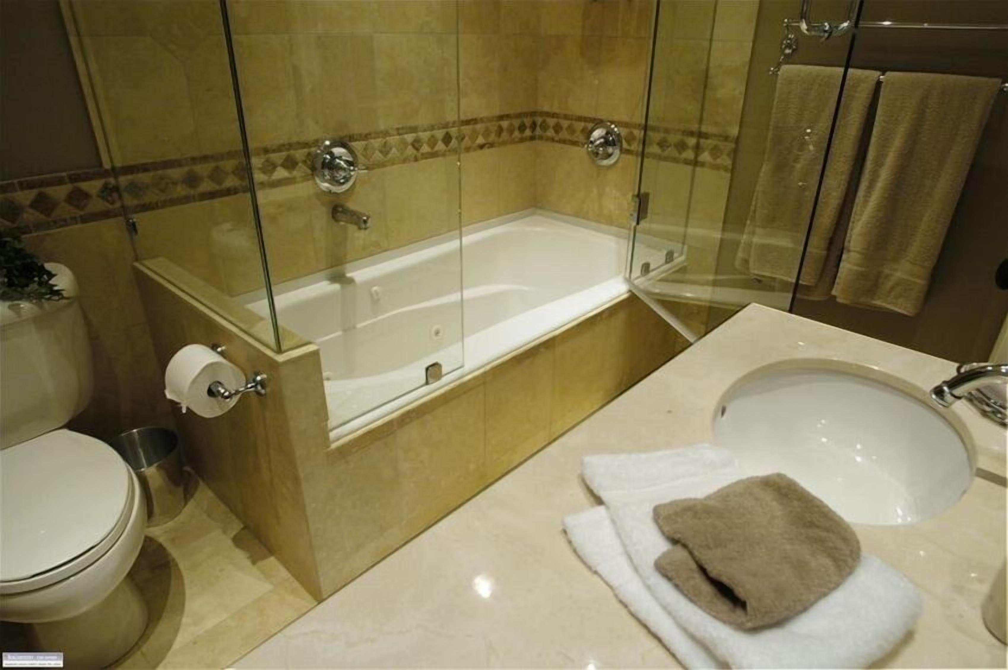 A bathroom with a glass-enclosed bathtub, a toilet, and a sink with towels.