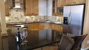 Een keuken met een centraal eiland, roestvrijstalen apparatuur, houten kastjes en een betegelde spatwand.