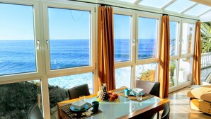 Un comedor con vista al océano a través de amplios ventanales, una mesa dispuesta con un cuenco, una taza y una piña.
