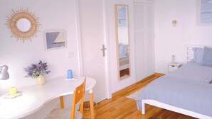 Un dormitorio con cama, mesita de noche, silla, escritorio, espejo y ventana.