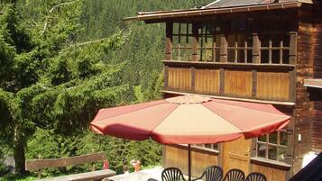 A wooden building with a terrace, outdoor seating, and a mountain view.
