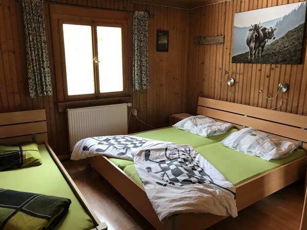 A wooden cabin room with a bed, a window, and a painting of cows on the wall.